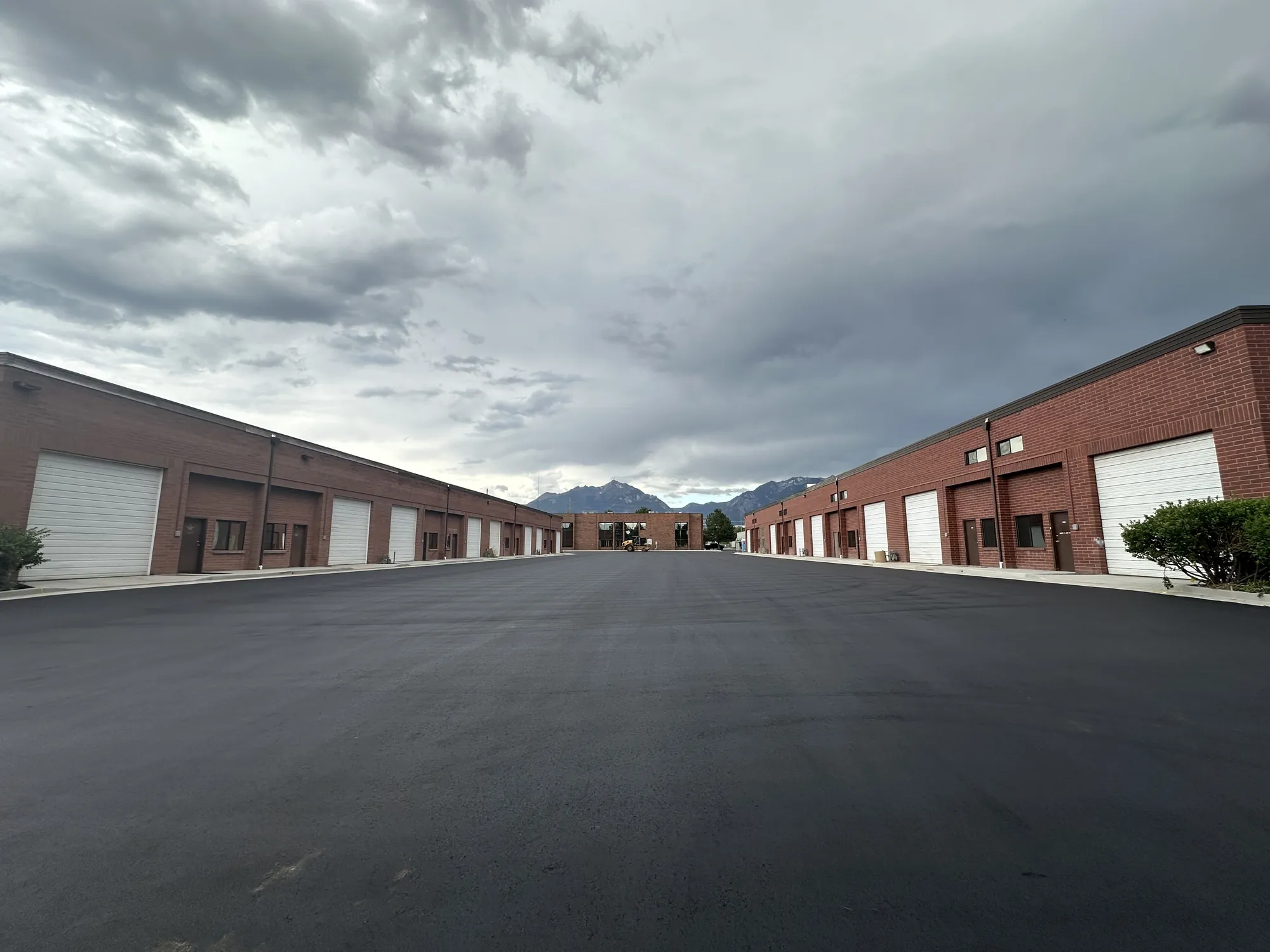 Two rows of red brick industrial units with roll-up doors, the Wasatch mountains behind